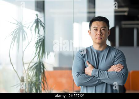 ritratto di uomo d'affari freelance asiatico in ufficio moderno, uomo con le braccia incrociate guardando seriamente la macchina fotografica Foto Stock