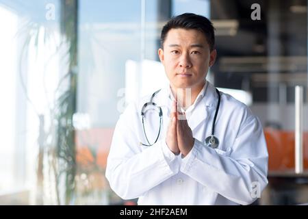 Medico asiatico serio guardando la webcam ascoltare il paziente interlocutore online, uomo che lavora da remoto dalla clinica Foto Stock
