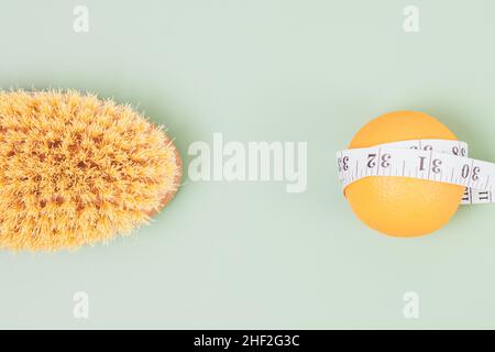 Concetto di massaggio con spazzola a secco anticellulite accanto all'arancio fresco e nastro di misurazione su sfondo chiaro, vista dall'alto Foto Stock