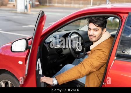 Ritratto di giovane uomo in giacca apre la porta dell'auto di giorno. Vista dall'esterno Foto Stock