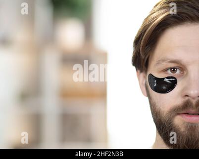 Bellezza maschile. Cura della pelle e trattamenti per la zona sotto gli occhi. Metà del volto del giovane bel bearded uomo caucasico con le macchie nere degli occhi, spazio libero della copia, primo piano Foto Stock