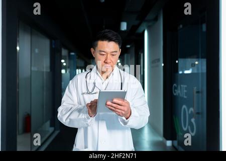 Medico asiatico serio, usa un computer tablet, l'uomo lavora in una clinica moderna Foto Stock
