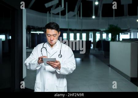Medico asiatico serio, usa un computer tablet, l'uomo lavora in una clinica moderna Foto Stock