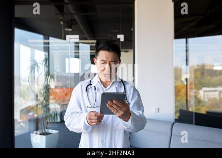 Medico asiatico serio, usa un computer tablet, l'uomo lavora in una clinica moderna Foto Stock