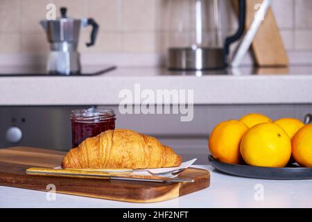 Croissant fresco e marmellata e piatto di arance si trovano sul tavolo da cucina Foto Stock
