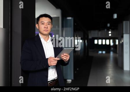 Serio lavoratore maschile asiatico si è concentrato sul lavoro di lavoro con computer tablet in un ufficio moderno Foto Stock