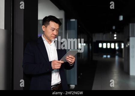 Serio lavoratore maschile asiatico si è concentrato sul lavoro di lavoro con computer tablet in un ufficio moderno Foto Stock