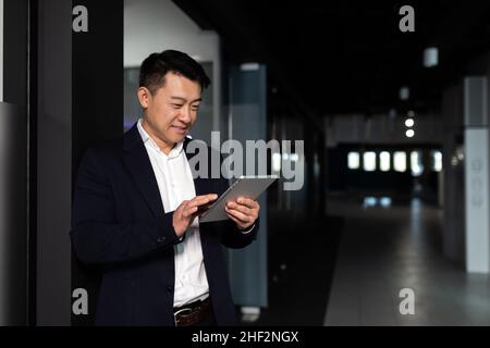 Serio lavoratore maschile asiatico si è concentrato sul lavoro di lavoro con computer tablet in un ufficio moderno Foto Stock