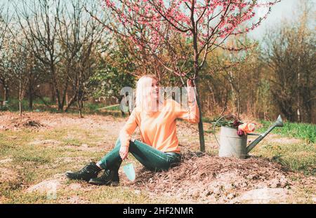 Giardiniere ragazza sul giardino di primavera. Concetto di giardinaggio della gente. Donna giardiniere felice con annaffiatura può. Foto Stock