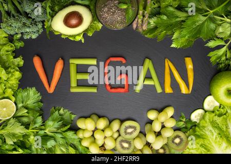 Vista dall'alto di verdure fresche verdi e frutta cornice con parola vegan su sfondo nero. Cibo vegano e concetto di dieta vegana Foto Stock