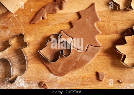 Tagliare le forme dalla pasta per pasticceria per preparare biscotti di Natale al pan di zenzero, vista dall'alto Foto Stock