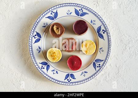 Mini dessert vegani crudi mirtillo, goji, lampone, limone e banana su un piatto decorato su sfondo bianco, vista dall'alto Foto Stock