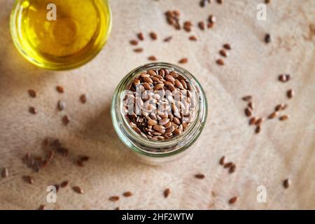 Semi di lino in un vaso di vetro e olio sullo sfondo, vista dall'alto Foto Stock