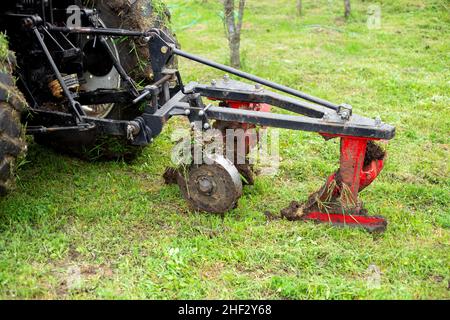 Trattore con un aratro su un campo rurale verde. Un dispositivo per arare il terreno nel giardino. Foto Stock