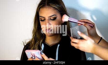 Il Teenager guardando il suo telefono, mentre il suo amico sta facendo il suo trucco Foto Stock