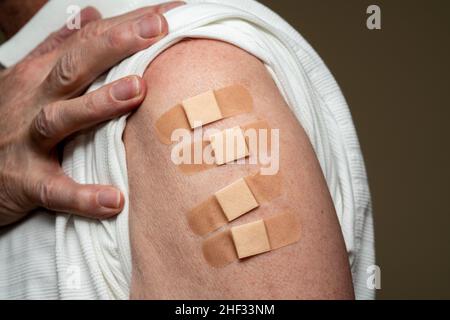 Manica da uomo caucasica senior per mostrare il quarto vaccino di richiamo per coronavirus sparato nella spalla. Concetto con quattro bende separate per gli shot Foto Stock