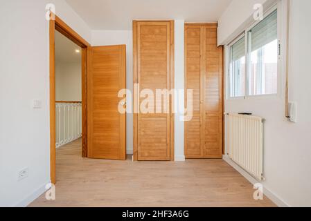 Camera da letto con armadi in ciliegio e porte veneziane e radiatore in alluminio bianco Foto Stock