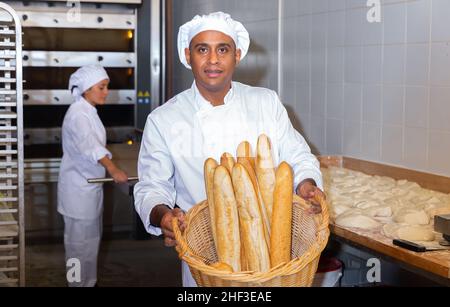 Panettiere ispanico che mostra baguette appena sfornate in panetteria Foto Stock