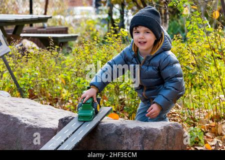 Ragazzo di due anni che gioca con il trattore giocattolo sulla rampa in sandbox parco città Foto Stock