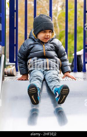 Ragazzo di due anni sul parco giochi della città slidboard Foto Stock