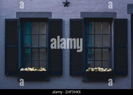 Finestre tradizionali con persiane di legno nero su una parete di mattoni grigi di un edificio di appartamenti Foto Stock