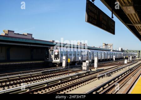 F treno della metropolitana che si avvicina alla stazione sopraelevata di Brooklyn, New York. Binari ferroviari sulla piattaforma all'aperto Foto Stock