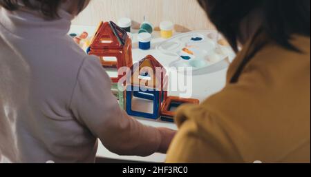 Il bambino con la madre raccoglie un costruttore magnetico, un primo scatto, una vista posteriore Foto Stock