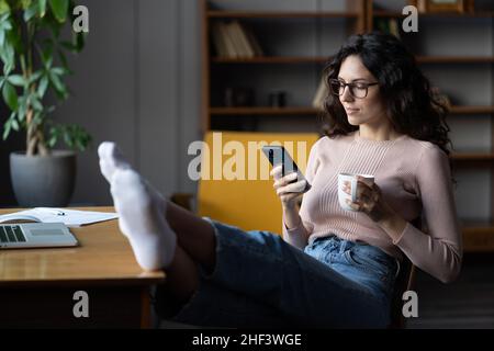Donna dipendente remoto procrastinate sul posto di lavoro leggere il testo nel cellulare distratto dal lavoro laptop Foto Stock