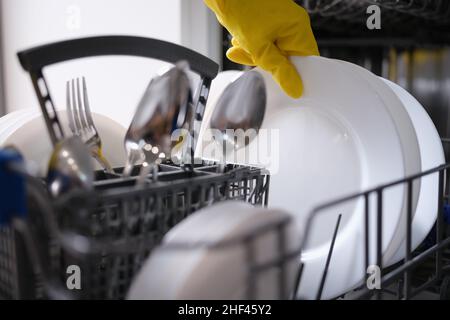 Una mano in un guanto giallo estrae i piatti dalla lavastoviglie Foto Stock