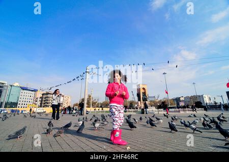 Una ragazza turca che corre e gioca tra i piccioni in piazza Taksim a Istanbul, Turchia. Foto Stock