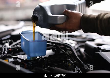 Versare l'olio della macchina attraverso un imbuto nel motore di un'auto, in primo piano. Cambio dell'olio, lubrificazione dei componenti del motore Foto Stock
