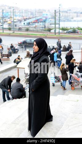 Una donna che indossa abaya in posa per una foto dello Yeni Cami in Piazza Eminonu, Istanbul, Turchia. Foto Stock