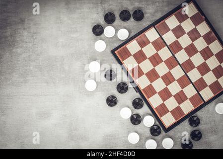 Le dama sono sparse vicino alla scacchiera, vista dall'alto. Giochi di mente, sviluppo mentale e strategia. Giochi per bambini e adulti. Scuola di scacchi. Foto Stock