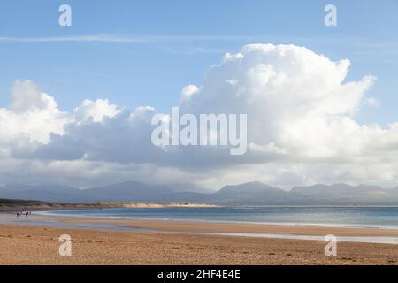 Persone che camminano sulla spiaggia di Newborough con le montagne Snowdonia sullo sfondo, Anglesey, Galles del Nord Foto Stock