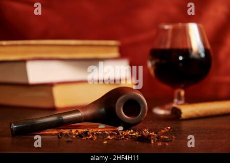 Un bicchiere di vino, sigaro, tabacco, pipa fumante, fiammiferi, libri sulla scrivania in legno. La vita morta con accessori di lusso Foto Stock