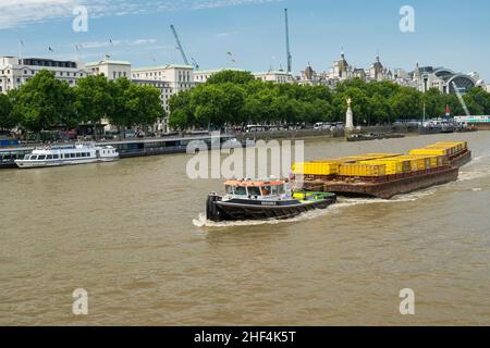 Cory Tugboat risorsa che salendo il fiume Tamigi tirando contenitori vuoti verso il ponte di Westminster con la Statua dell'Aquila d'Oro del RAF Memorial. Foto Stock