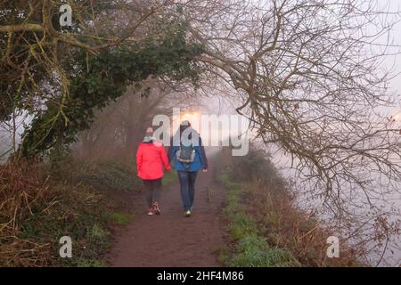 Wareham, Dorset Regno Unito. 14th gennaio 2022. Tempo britannico: Un freddo inizio a Wareham, Dorset come nebbia appende sopra il fiume Frome al mattino. Una coppia fa una passeggiata lungo il fiume. Credit: Carolyn Jenkins/Alamy Live News Foto Stock