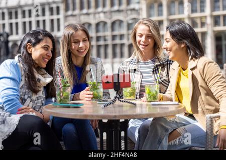 Anversa, Belgio, 21 maggio 2021, quattro turisti o studenti di razza mista seduti fuori nel centro storico della città in una caffetteria terrazza con una videochiamata utilizzando il telefono cellulare. Foto di alta qualità Foto Stock