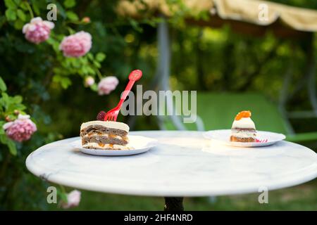 un pezzo di torta di frutta fatta in casa servito su un tavolo di marmo sullo sfondo di un giardino con rose in fiore - fuoco selettivo Foto Stock