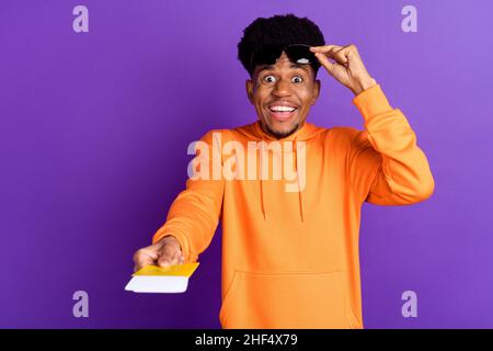 Foto di giovane felice afro americano uomo tenere mani biglietto vi danno viaggio isolato su sfondo di colore viola Foto Stock