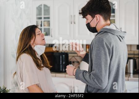 Ragazzo adolescente che prende il test PCR da madre a casa durante la pandemia di COVID Foto Stock
