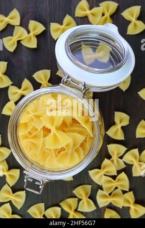 Vista dall'alto della pasta secca di Farfalle in un vaso di vetro aperto con alcuni sparsi intorno Foto Stock