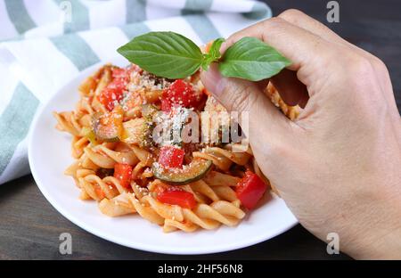 Mettere a mano le foglie di basilico su un piatto di farina di grano fresco cotto Fusilli Pasta in salsa di pomodoro Foto Stock