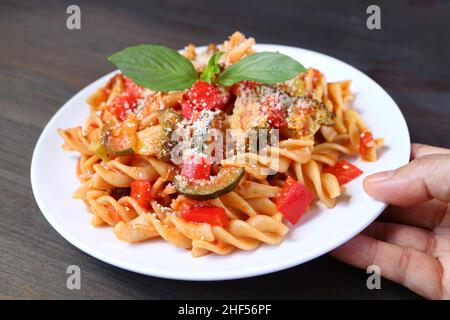 Mano mettendo un piatto di succulenta pasta di Fusilli integrale in salsa di pomodoro su tavola di legno Foto Stock