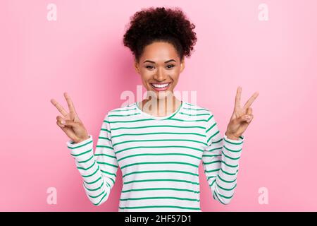 Foto di bella capelli ondulati millennial donna mostra v-segno indossare camicia a righe isolato su sfondo rosa Foto Stock