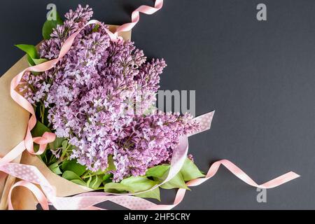 Bouquet di fiori di lilla con nastri su sfondo scuro. Cartolina con spazio per il testo. Foto orizzontale. Foto Stock