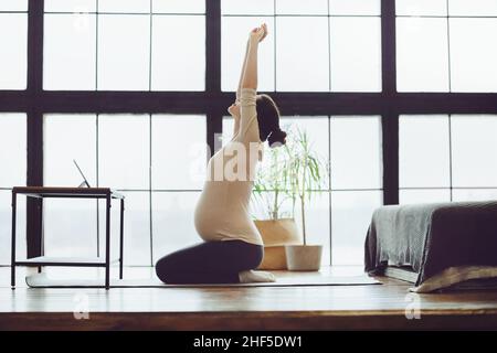 Tutta la lunghezza di giovane calma donna incinta che fa yoga in linea a casa, guardando lo schermo digitale del tavolo e facendo esercizi di stretching, lif sano Foto Stock