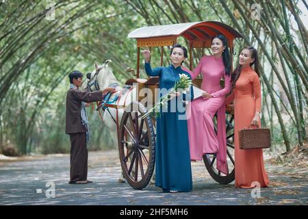 Ho Chi Minh City, Viet Nam: Le ragazze vietnamite indossano ao dai bianco e cavalcano su una carrozza trainata da cavalli su una strada di campagna in Vietnam Foto Stock