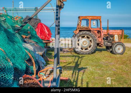 attività stagnante e noiosa nel settore della pesca: illustrazione con un vecchio trattore agricolo e reti da pesca inutilizzate in riva al mare da trainare verso l'oceano Foto Stock