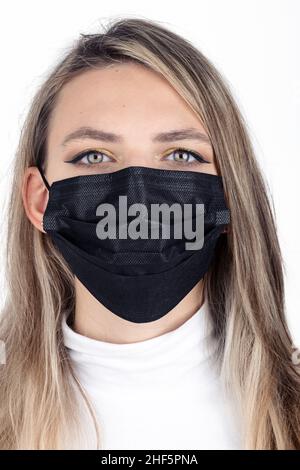 Concetto di medicina e assistenza sanitaria. Primo piano giovane e lungo capelli brunette donna ritratto con maschera medicina nera sul suo viso isolato su bianco backgroun Foto Stock